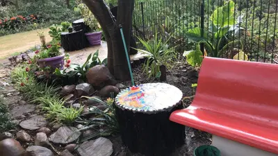 a red bench in a garden with a tree stump at ilyn pottery cottage in Pretoria