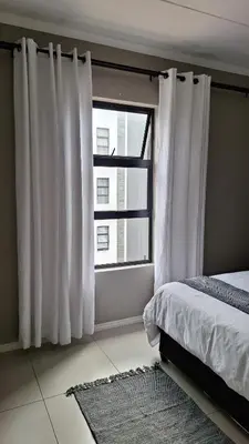 a bedroom with a bed and a window with white curtains at Luxury Apartments in Midrand
