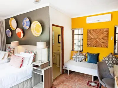 a bedroom with yellow walls and a bed and a mirror at Sabores Lodge and Restaurant in Nelspruit