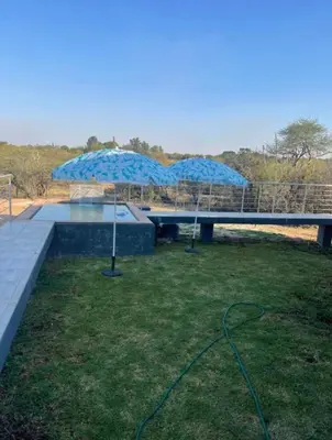 a patio with a blue umbrella on the grass at Kings view exclusive villas in Petronella