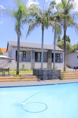 a house with palm trees in front of a swimming pool at Nouvelle Ere Beauty Spa & Boutique Guesthouse in Centurion