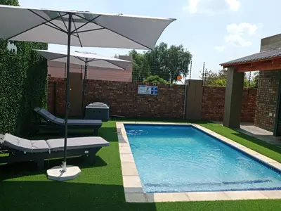a swimming pool with an umbrella and a chair and a table at Lavani Lodge in Lerulaneng