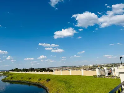 a river with a fence and a blue sky with clouds at Lake view Apartment and suite in Midrand