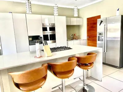 a kitchen with a white counter and brown chairs at Lake Villa Hartebees in Hartbeespoort