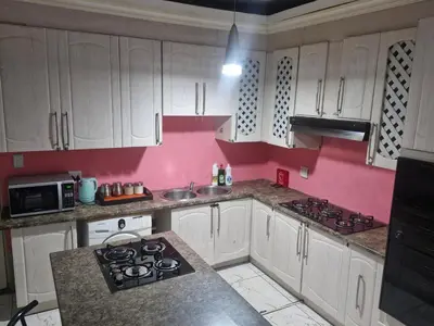 a kitchen with white cabinets and a pink wall at AB Lisi Accommodation in Pretoria