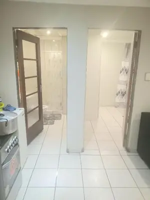 a bathroom with a white tiled floor and an open door at Kama house in Pretoria