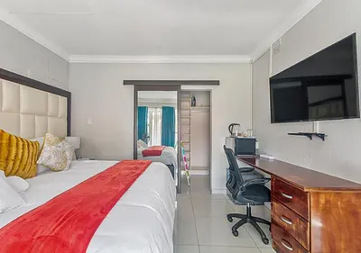 a hotel room with a bed and a desk and a tv at The Golden Place in Kempton Park