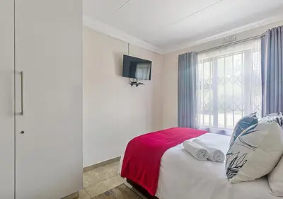a bedroom with a bed with a red blanket and a window at The Golden Place in Kempton Park