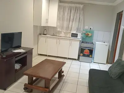 a kitchen with white cabinets and a table and a tv at Kama B&B in Pretoria