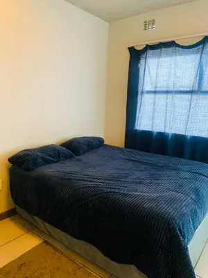 a bedroom with a bed with a blue comforter and a window at Luxury Park Stays in Midrand