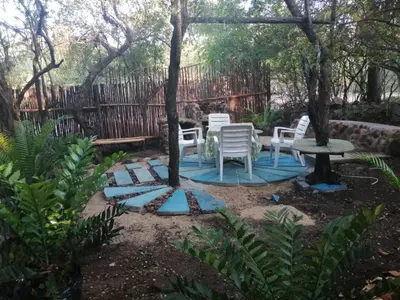 a patio with white chairs and a table and trees at Gemsbokrus in Marloth Park