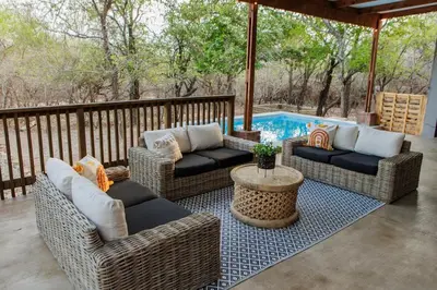 a patio with wicker chairs and a table and a pool at Chawal Stays Ribbok in Marloth Park