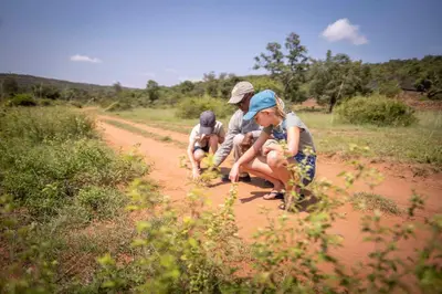three children are sitting on a dirt road at Ekuthuleni Lodge in Welgevonden Game Reserve