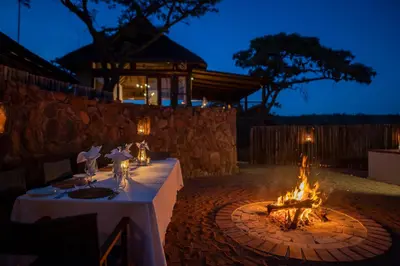 a table with a fire pit in a backyard at night at Ekuthuleni Lodge in Welgevonden Game Reserve
