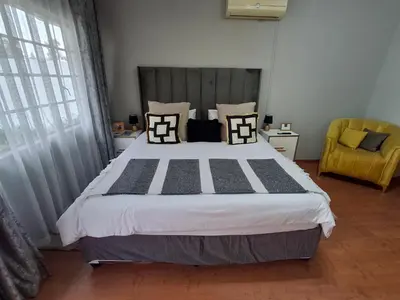a bedroom with a large bed and a yellow chair at 118 Bayley Street in Benoni