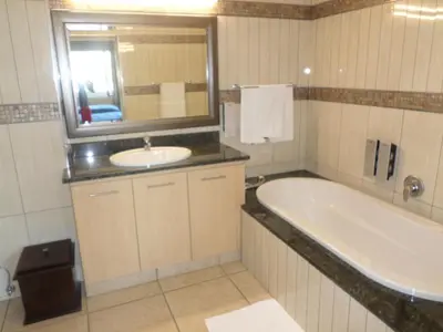 a bathroom with a tub and a sink and a mirror at The Links Guest House in Pretoria
