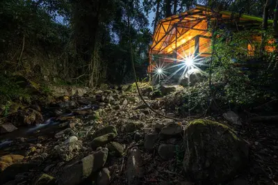 a lit up building in the woods next to a river at Matumi Trail Forest Lodges - Matumi and Mitzeeri in Tzaneen