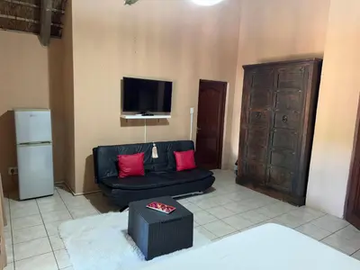 a living room with a black couch and a tv at VM Guesthouse in Hazyview