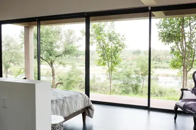 a bedroom with a large window with a bed and a chair at Ziziphus River Lodge in Hectorspruit