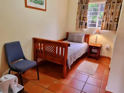 a bedroom with a bed and a chair and a window at Harties Is Africa Safari Lodge in Hartbeespoort