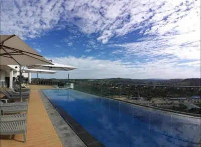 a large swimming pool with chairs and an umbrella at 418 menlyn Maine trilogy in Pretoria