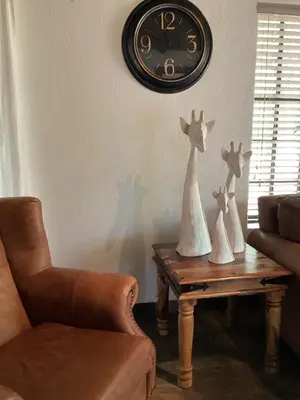 a living room with a clock on the wall and a table at Sounds of Kruger Safari Villa in Marloth Park