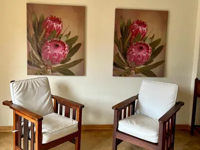 two chairs in a room with two paintings on the wall at Karee Guesthouse in Thabazimbi