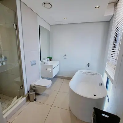 a white bathroom with a tub and a toilet at Ellipse Waterfall luxurious and modern apartment in Midrand