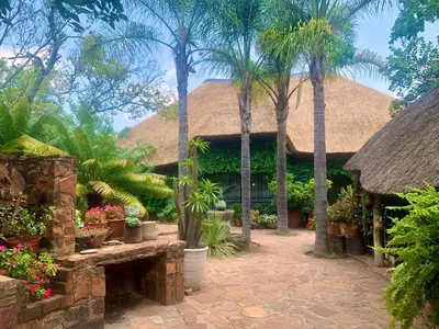 a resort with palm trees and a thatch roof at Hermit Hill in Broederstroom