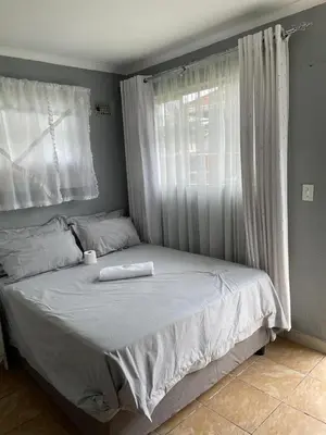 a bedroom with a bed with white sheets and a window at comfort zone in Kempton Park