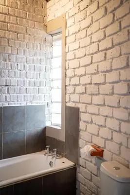 a bathroom with a white brick wall and a bath tub at Ngoma Bush Lodge in Hoedspruit