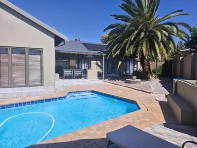 a swimming pool in front of a house with a palm tree at Nightingale Lodge Bed and Breakfast in Kempton Park