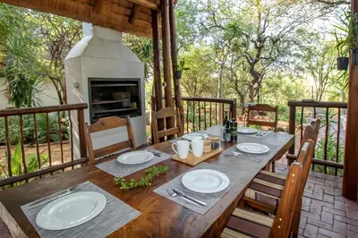 a wooden table with chairs and a fireplace on a porch at Woodlandsbushlodge in Hoedspruit