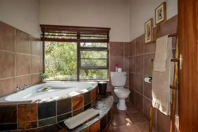 a bathroom with a tub and a toilet and a window at Woodlandsbushlodge in Hoedspruit