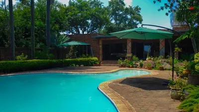 a swimming pool with an umbrella and a house at Kneizenberg Boutique Lodge & Spa in Louis Trichardt