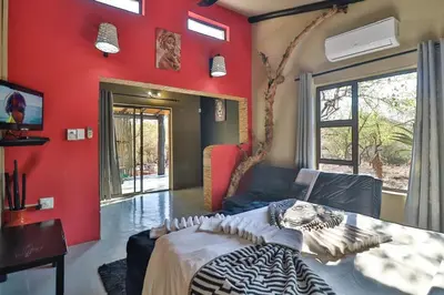 a bedroom with a red wall with a bed and a couch at Shiringa kruger lodge in Marloth Park