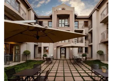 a patio with tables and umbrellas in front of a building at Cozy Apartment in Hatfield in Pretoria