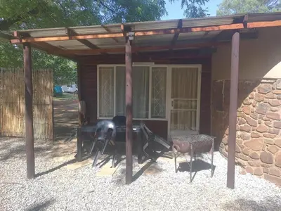 a wooden pergola with a table and chairs in front of a building at Cottage 3 at Cynthias Country in Hartbeespoort