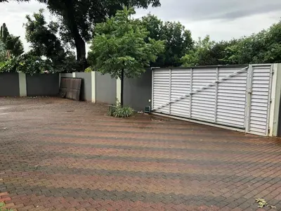 a driveway with a white gate and a tree at Tranquility in the Trees Loft Style Apartment in Pretoria