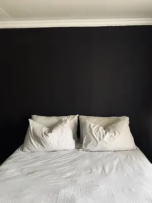 a bed with white pillows against a black wall at The Ripanga Nest in Nelspruit