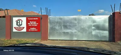 a metal wall in front of a building with a sign at Emlomo logde in Ermelo
