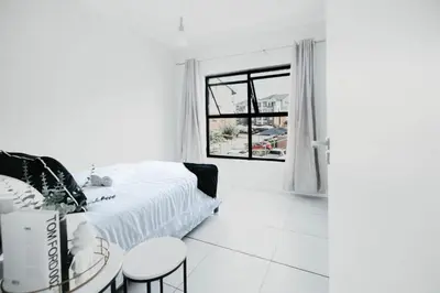 a white bedroom with a bed and a table and chairs at The Blyde Crystal Lagoon Apartment in Pretoria