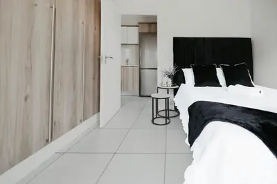 a white bedroom with a large bed and a table at The Blyde Crystal Lagoon Apartment in Pretoria