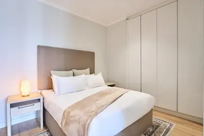 a white bedroom with a large bed and a night stand at MaZZ at Ellipse Waterfall in Midrand