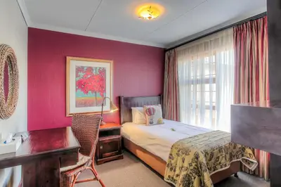 a bedroom with a bed and a desk and a window at Sunninghill Guest Lodges in Johannesburg
