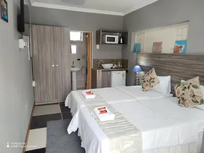 a bedroom with a large white bed and a kitchen at DAMOFUS Guest House in Pretoria