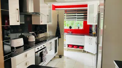 a kitchen with white cabinets and a red wall at Yvee Guesthouse in Hazyview