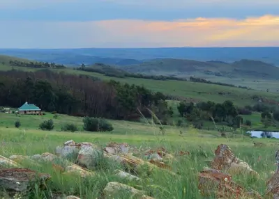 a field of grass with rocks and a house in the distance at Kwaggaskop Game Farm - near Dullstroom in Belfast