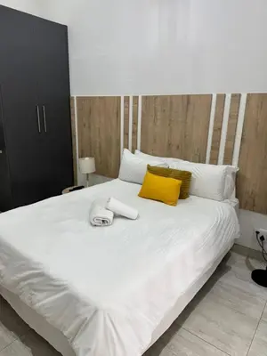 a white bed with a yellow pillow and a phone on it at Kioma Guest House in Mokopane