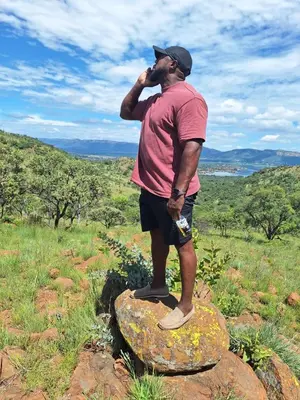 a man standing on a rock talking on a cell phone at Chalet 3 at Cynthias Country in Hartbeespoort